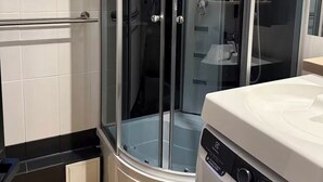 Een moderne badkamer met een douche met glazen wand, een inbouwwastafel en een wasmachine.