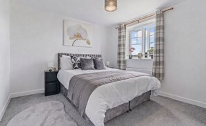 Quarto com cama, mesa de cabeceira e janela com cortinas.