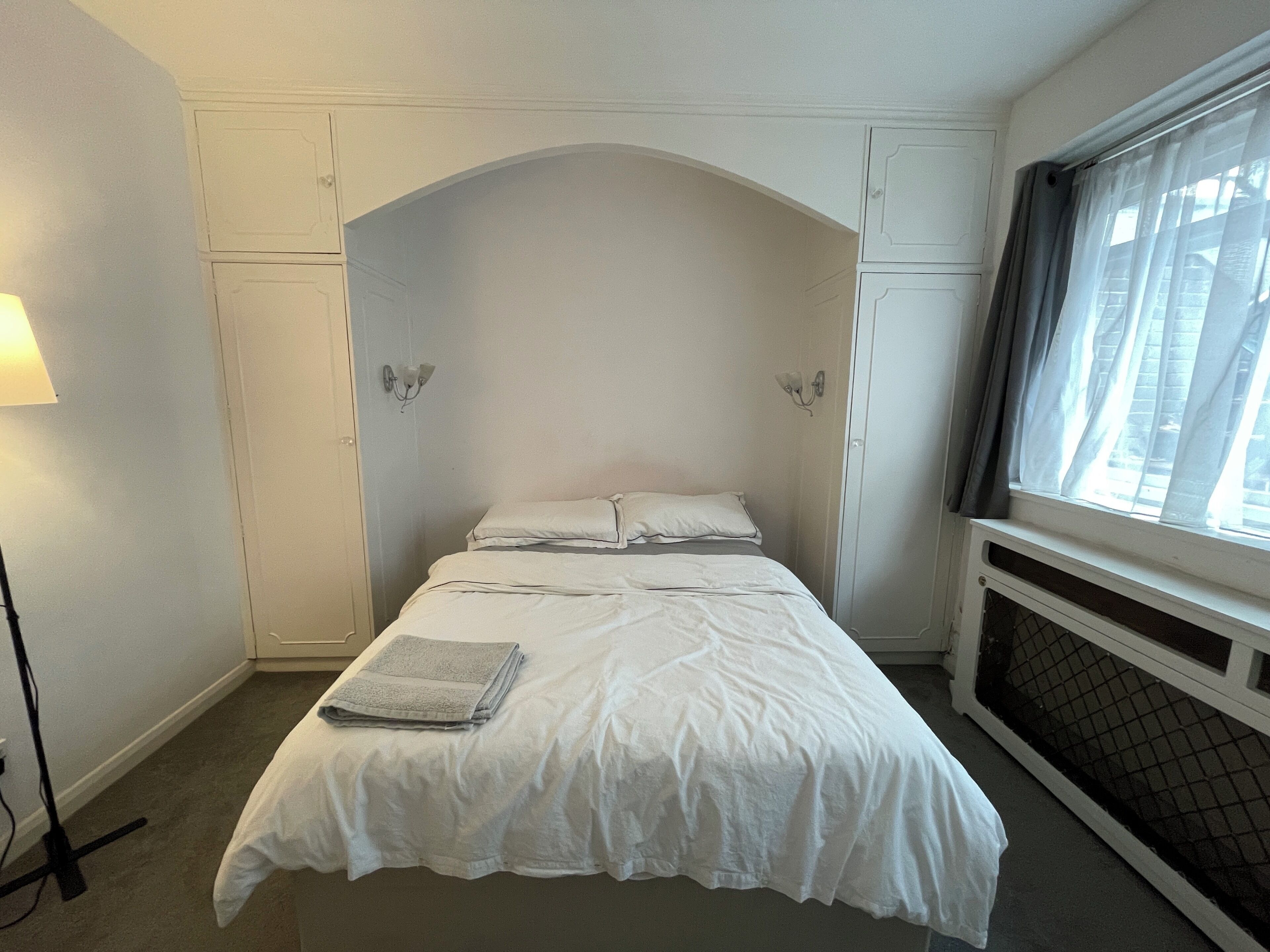 Un dormitorio con cama, ventana con cortinas y radiador.