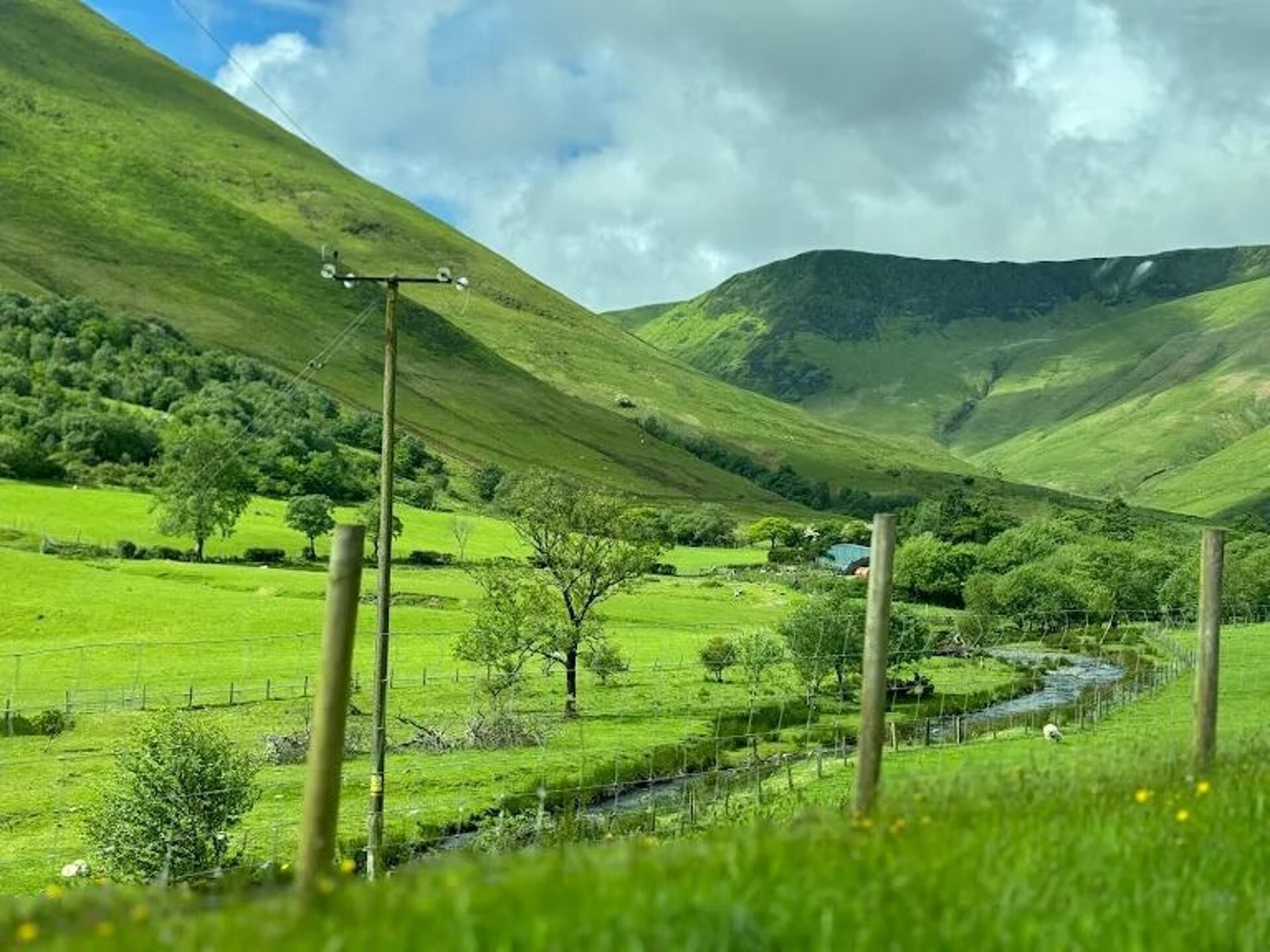 Paisaje rural con colinas onduladas, un arroyo y una cerca.