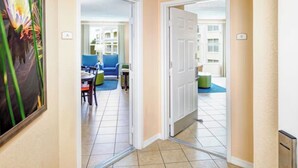 A hotel corridor with a tiled floor, a painting of a flower, and a door leading to a room with a blue chair and a table. - Resort-Style 2BR Condo-7 Pools, Hot Tubs & Family Amenities minutes from Disney (Kissimmee)
