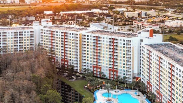 A high-rise hotel with multiple floors, a central swimming pool, and a surrounding landscaped area. - Resort-Style 2BR Condo-7 Pools, Hot Tubs & Family Amenities minutes from Disney (Kissimmee)