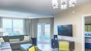 A modern hotel room with a sofa, chairs, a glass table, a TV, and a balcony with curtains. - Resort-Style 2BR Condo-7 Pools, Hot Tubs & Family Amenities minutes from Disney (Kissimmee)