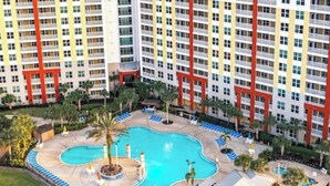 A hotel with a large swimming pool, multiple lounge areas, and a high-rise building in the background. - Resort-Style 2BR Condo-7 Pools, Hot Tubs & Family Amenities minutes from Disney (Kissimmee)