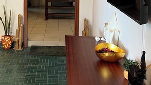 A room with a wooden door, a television mounted on the wall, a dining table with a bowl, and a potted plant. - Tropical duplex by the sea (direct private access) (Libreville)