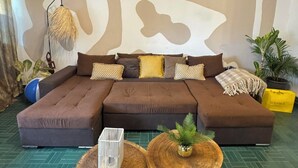 A sectional sofa with multiple cushions, two round wooden tables with plants, and a patterned wall. - Tropical duplex by the sea (direct private access) (Libreville)