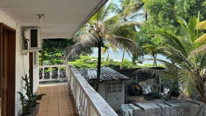 A covered balcony with a view of palm trees and a building with a tiled roof. - Tropical duplex by the sea (direct private access) (Libreville)