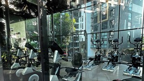 A gym with various exercise equipment, including treadmills and stationary bikes, in a modern building with large windows. - BKK Oasis Stylish & Cozy Condo Near MRT 200m (Bangkok)