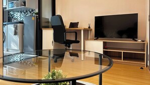 A modern office space with a glass table, a black office chair, a flat-screen TV, a refrigerator, and a kitchen area with a tiled backsplash. - BKK Oasis Stylish & Cozy Condo Near MRT 200m (Bangkok)