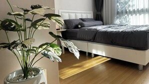 A modern bedroom with a bed, a potted plant, and a window with curtains. - BKK Oasis Stylish & Cozy Condo Near MRT 200m (Bangkok)
