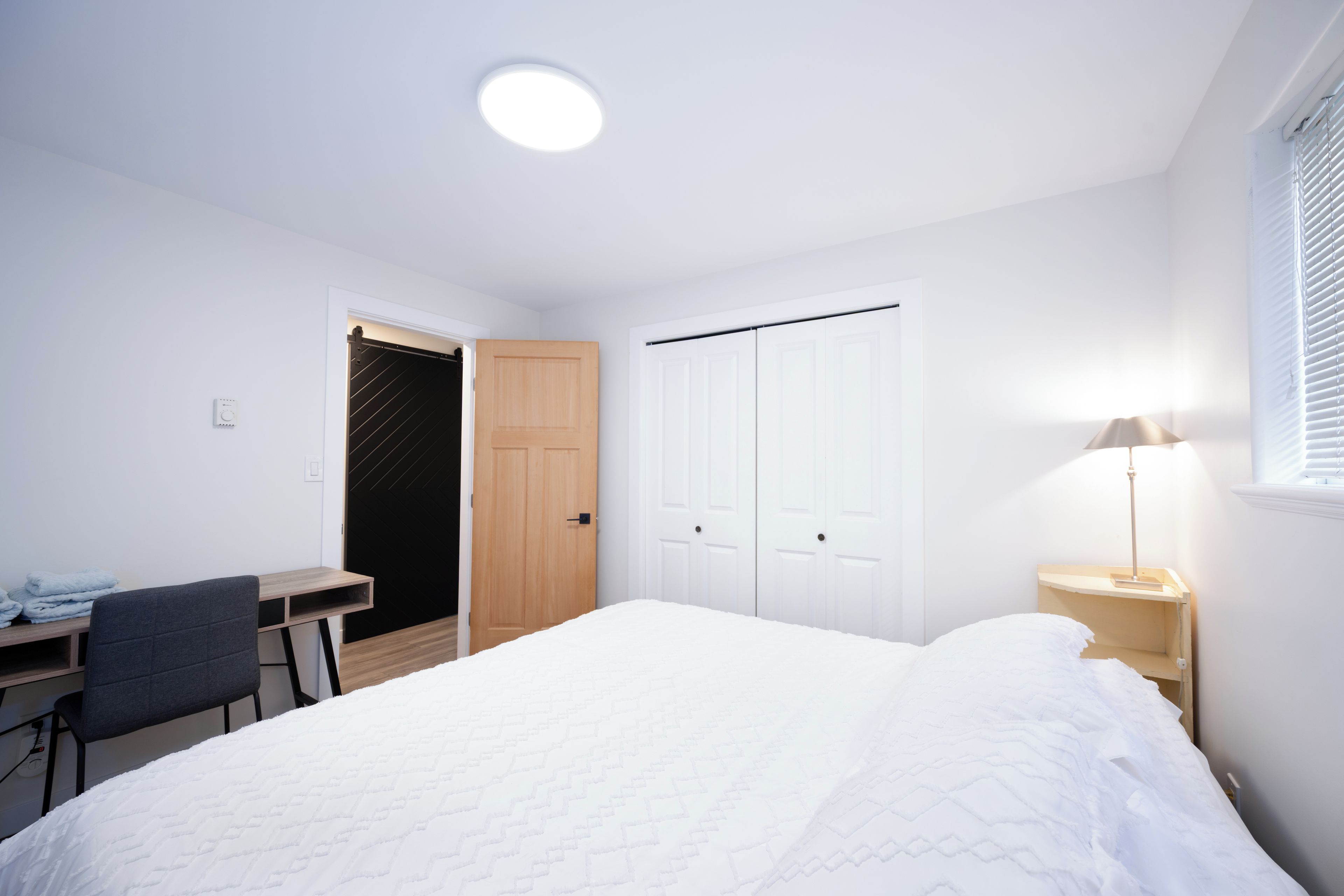 A bedroom with a bed, a desk, a chair, a wardrobe, and a bedside lamp.