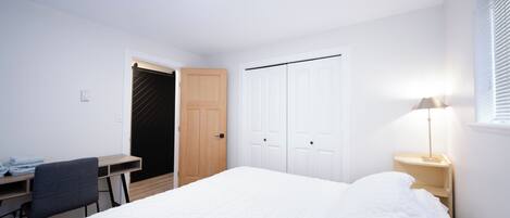 A bedroom with a bed, a desk, a chair, a wardrobe, and a bedside lamp.