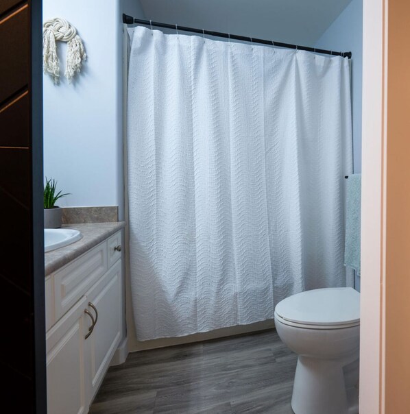 Une salle de bain équipée d’un rideau de douche, de toilettes, d’un lavabo et d’un porte-serviettes.