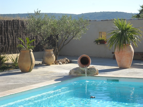 A swimming pool with a water spout, surrounded by potted plants and a view of hills. - HOUSE SWIMMING POOL GARDEN AIR-CONDITIONING ALL COMFORTS PETS ALLOWED AND GAMES FOR CHILDREN (Le Pouget)