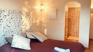 Een slaapkamer met een decoratief hoofdbord, een bed met kussens, een wandlamp en een douche.