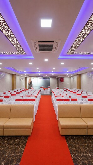 A conference room with rows of white chairs, a red carpet, and a patterned ceiling design. - Hotel Hyfa Continental (Lucknow)