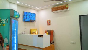 A reception desk with a ceiling fan, a mounted TV, and an air conditioning unit. - AVR Hotel (Indore)