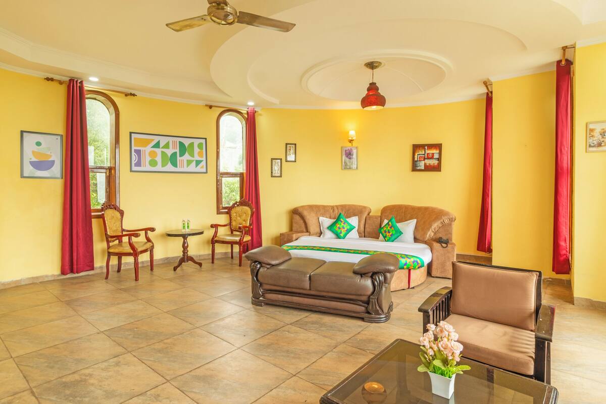 A room with a sofa, chairs, a table with flowers, a ceiling fan, and artwork on the walls.