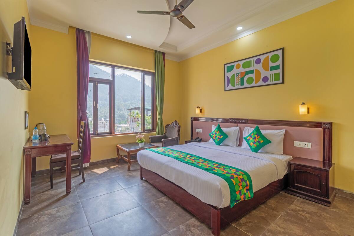 A hotel room with a bed, a desk, a chair, a window with a view, and a ceiling fan.
