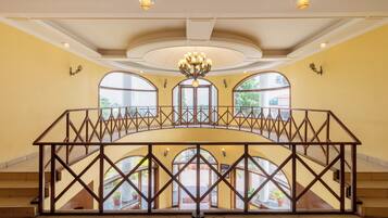 A spacious interior with a central balcony, large arched windows, and a chandelier.