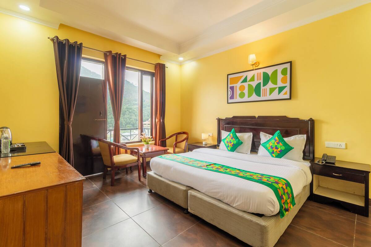 A hotel room with a bed, a desk, a chair, a nightstand, and a window with curtains.