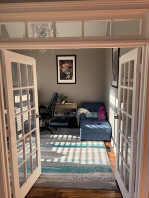 A room with a desk, chair, couch, and a framed picture on the wall.