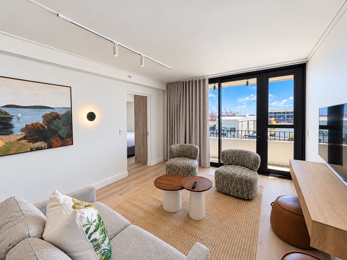 A modern hotel room with a large window, a painting, a sofa, a coffee table, and a TV.