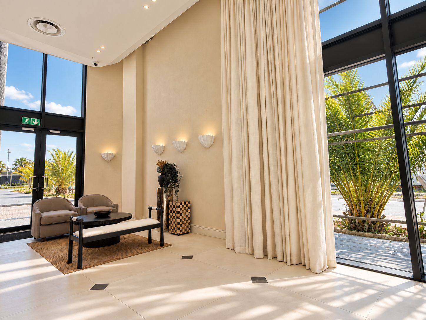 Un vestíbulo moderno con mostrador de recepción, zona de estar y amplias ventanas que ofrecen vistas a palmeras.