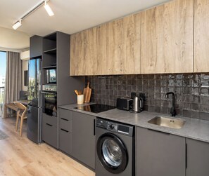 Una cocina moderna con armarios grises, lavadora integrada, pileta de acero inoxidable y salpicadero de madera.