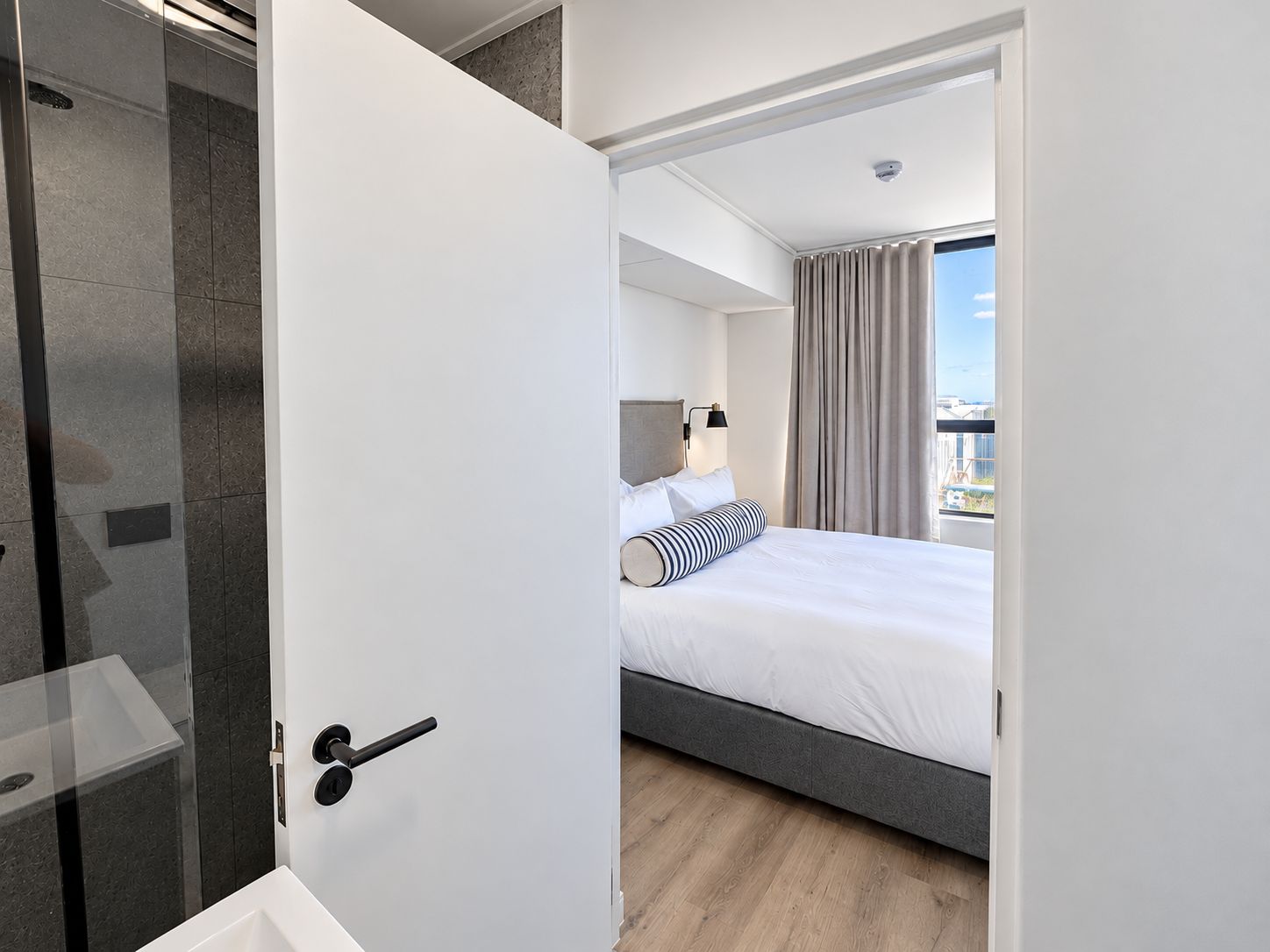 A modern hotel room with a bed, a bedside lamp, and a view of the city.