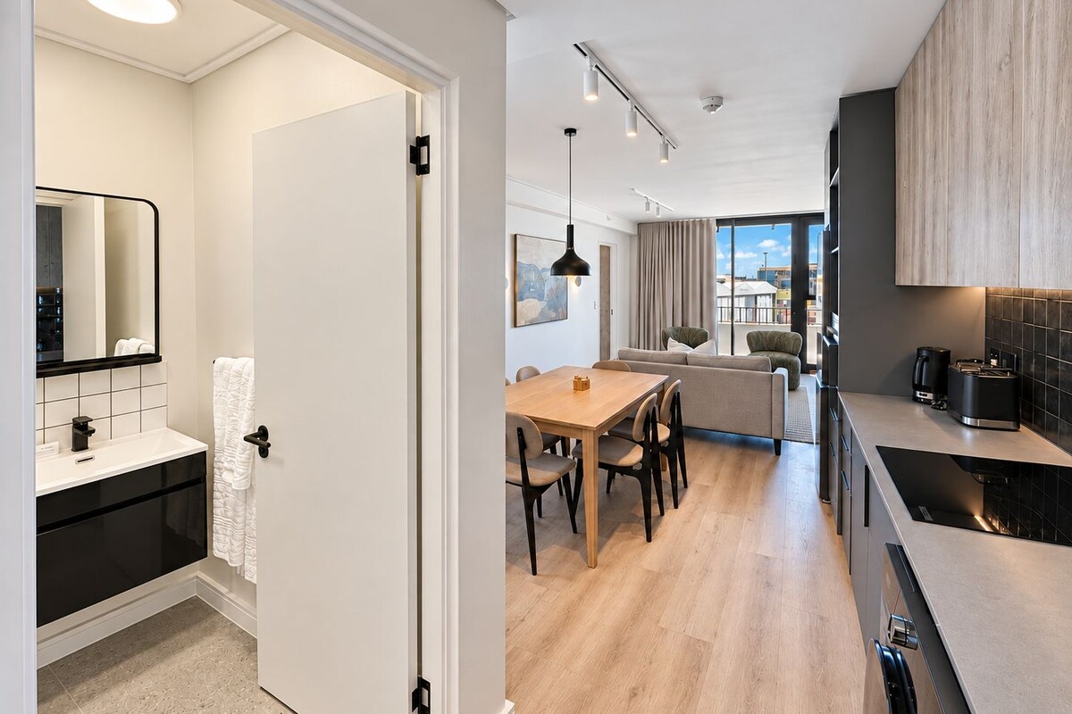 A modern apartment with a kitchen, dining area, and a living room with a sofa and chairs.