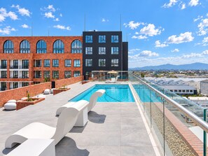 Zona de piscina en la azotea con piscina moderna, sillas de descanso y vistas a un paisaje urbano.