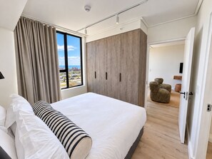 A modern hotel room with a large bed, a wardrobe, and a view of the cityscape. - Maritime Place (Cape Town)