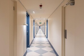 Un largo y estrecho pasillo de hotel con suelo a cuadros, puertas a ambos lados e iluminación en el techo.