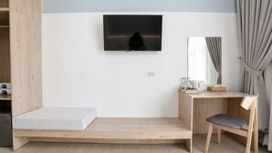 Une chambre avec un lit, un bureau et une chaise, un téléviseur fixé au mur et une fenêtre avec des rideaux.