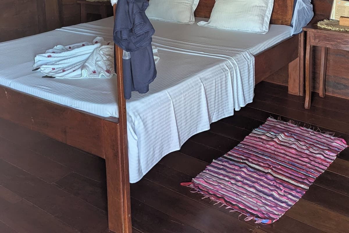 Una cama con dosel de madera con ropa de cama y almohadas blancas, un cabecero de madera y una mesita de noche con un libro.
