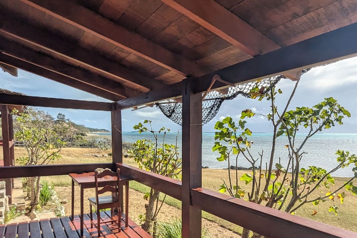 Una terraza de madera con un banco, una mesa y vistas a la playa y al océano.