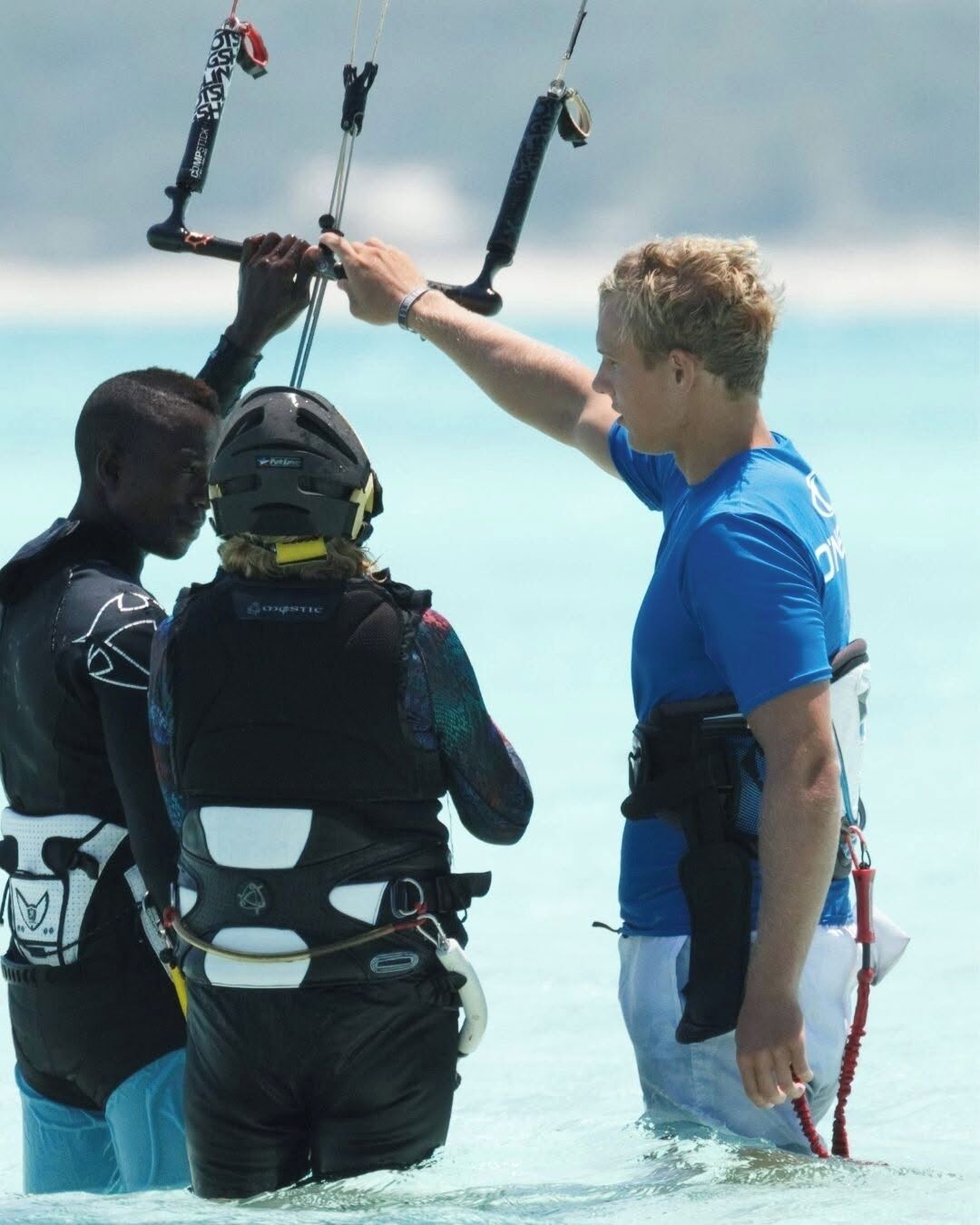 A person in a blue shirt and black vest standing in shallow water, holding a red rope.