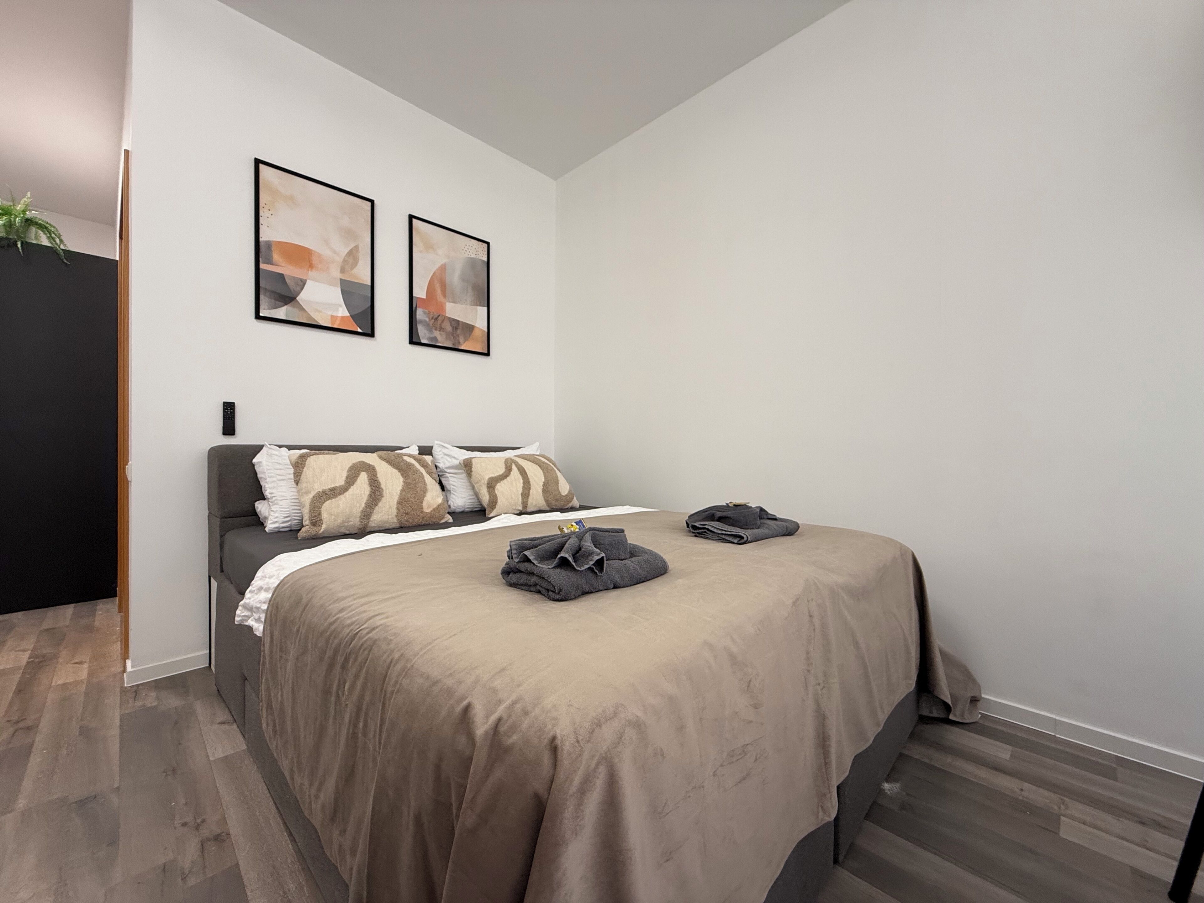 A modern bedroom with a bed, two abstract paintings, a remote control, and a folded towel on the bed.