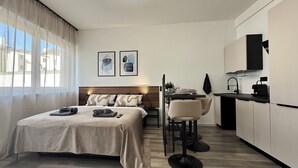 Quarto de hotel moderno com cama, escrivaninha e cozinha compacta.