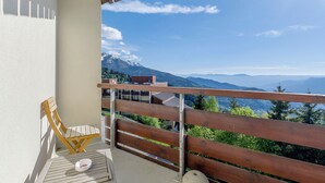A balcony with a wooden chair, a small table, and a view of snow-capped mountains. - Studio "Location Prapoutel" with Mountain View and Balcony (Les Adrets)