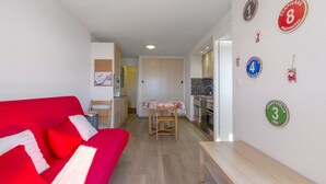 A compact living space with a red sofa, a wooden dining table, and a kitchenette. - Studio "Location Prapoutel" with Mountain View and Balcony (Les Adrets)
