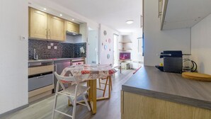 A compact kitchen with wooden cabinets, a tiled backsplash, a dining table with chairs, and a small island with a coffee machine. - Studio "Location Prapoutel" with Mountain View and Balcony (Les Adrets)