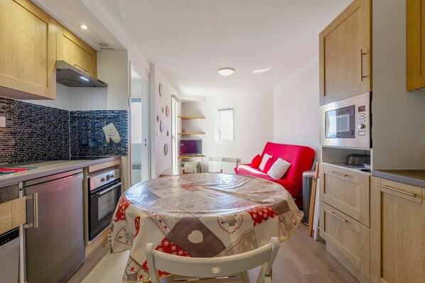A compact kitchen with a dining table, a microwave, and a red chair.