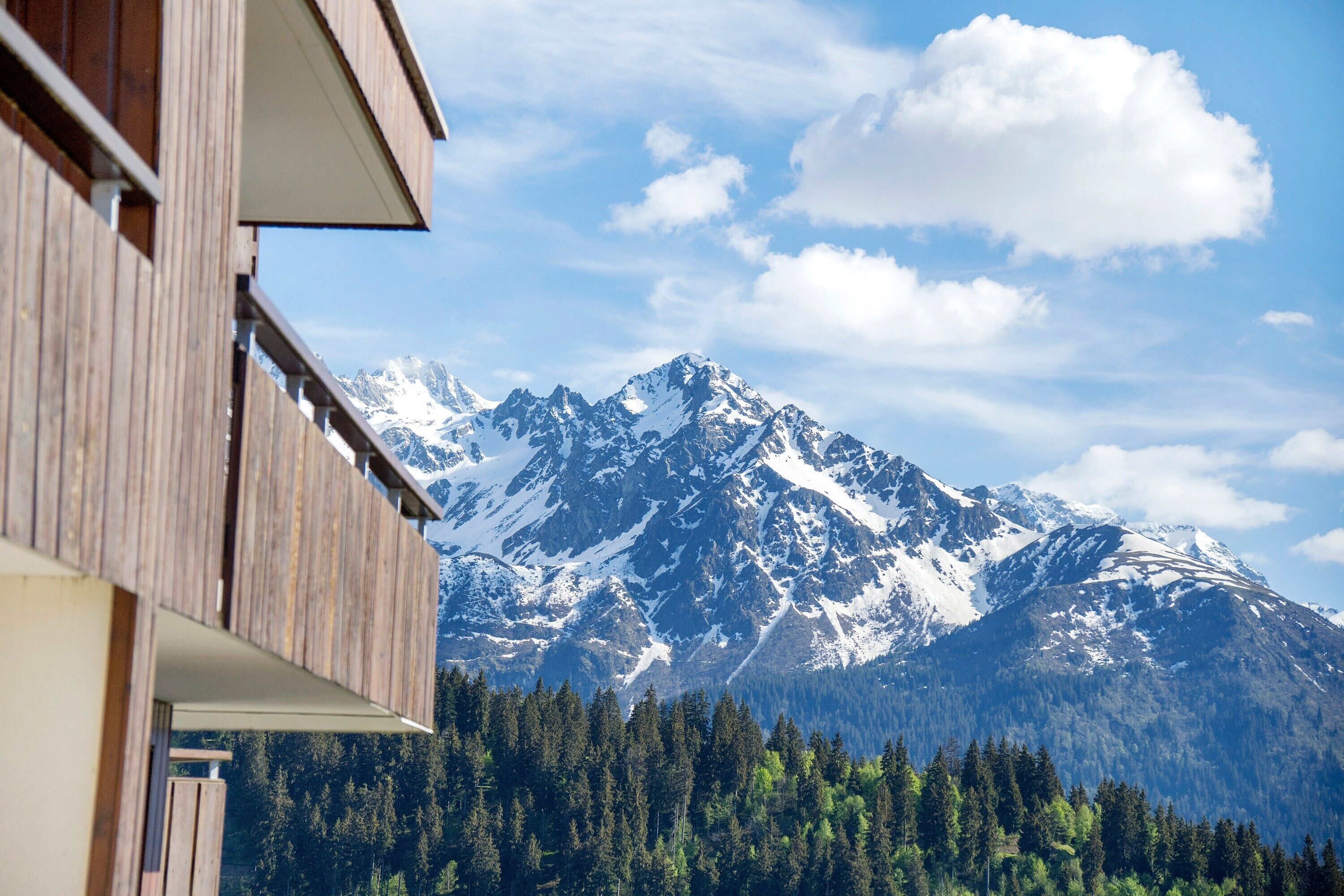 Un bâtiment en bois doté d’un balcon donnant sur des montagnes enneigées et une vallée boisée.