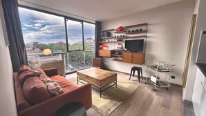 Uma sala de estar moderna com sofá, mesa de jantar e área de cozinha, incluindo televisão e prateleiras.