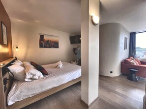 A hotel room with a bed, a cityscape painting, a television, and a seating area with a couch and a chair. - The Manhattan · Jean-Jaurès · Walk to Capitole (Toulouse)