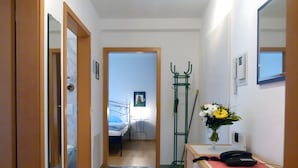 A hallway with a bed, a desk with a phone, a mirror, and a vase of flowers. - Apartment 'Am Lindenhof' with Balcony and Wi-Fi (Lindau (Bodensee))