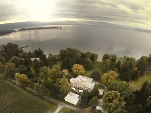 An aerial view of a large estate with a prominent building surrounded by dense trees and a body of water.