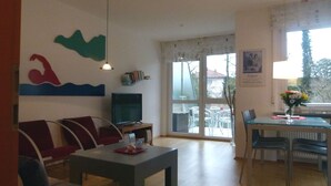 A living room with a television, a dining table with chairs, a sofa, and a window with a view of the outside. - Apartment 'Am Lindenhof' with Balcony and Wi-Fi (Lindau (Bodensee))